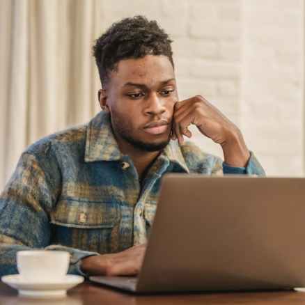 concentrated young black guy sitting at table and working remotely on netbook