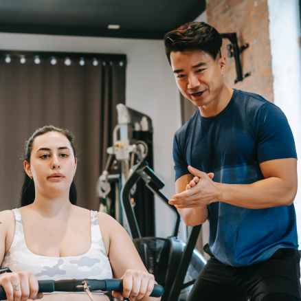 smiling ethnic coach clapping hands to overweight female in gym